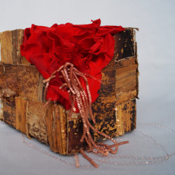 Composition en cube de carton dur, fibre de bananier, pétales de roses rouges et fil doré